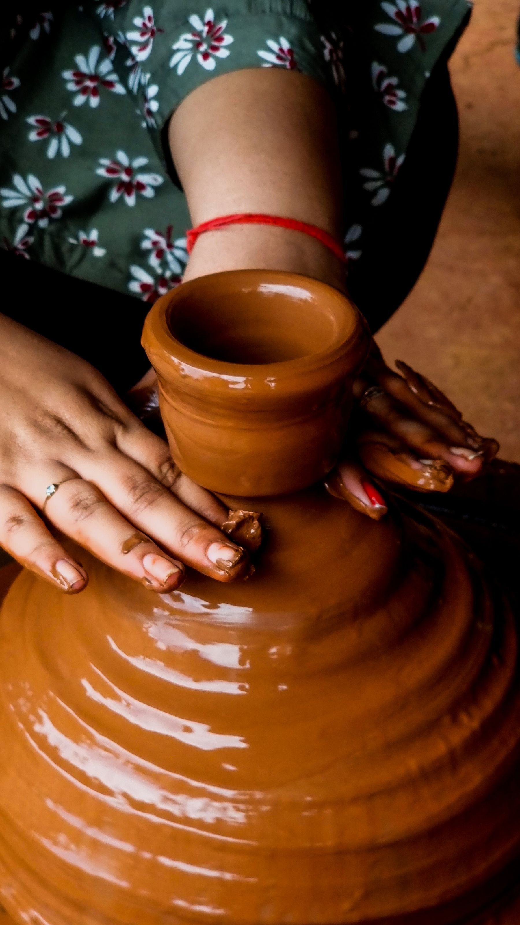 Illustrative photograph: Hands shaping a terracotta vessel on a pottery wheel.