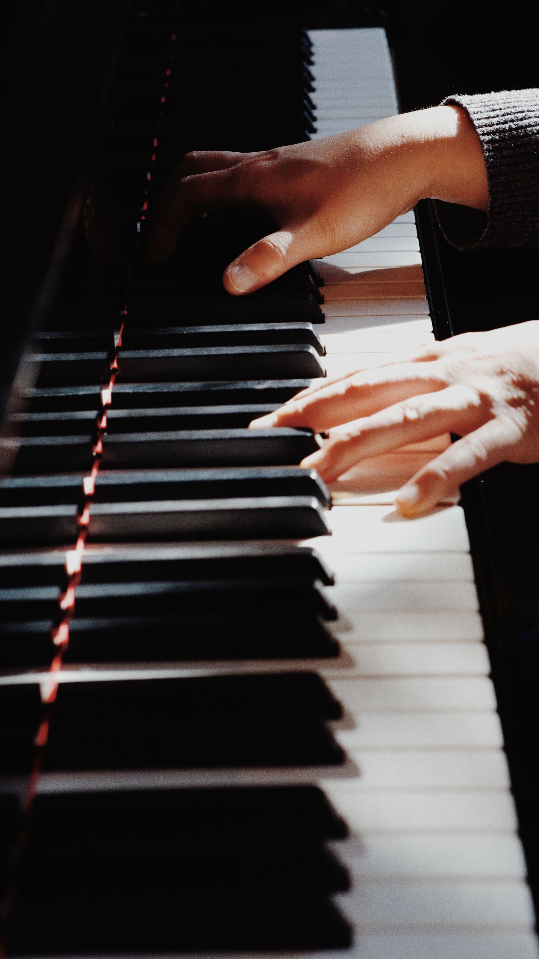 Illustrative photograph: A close view of hands playing the polished keys of a piano.
