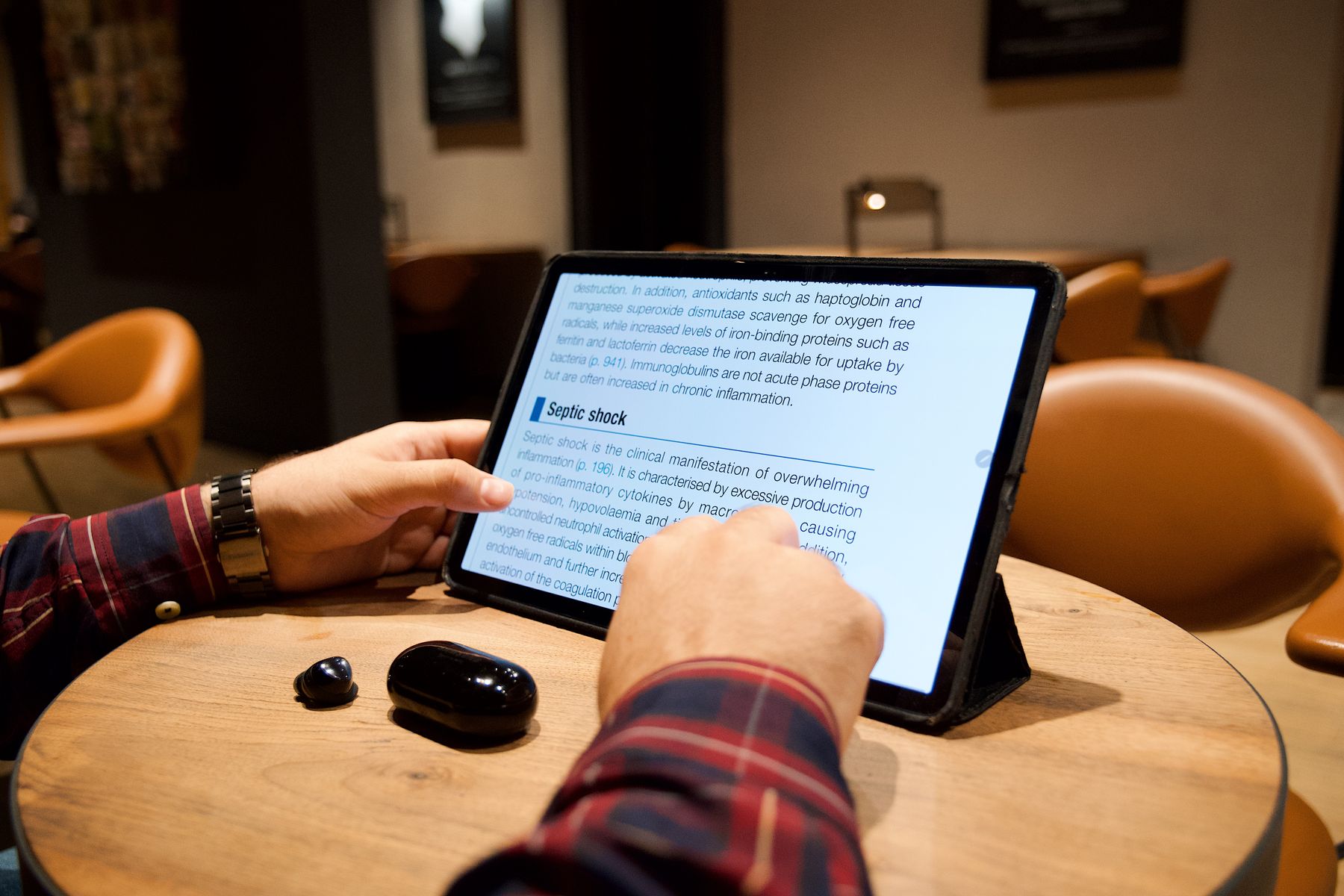 Illustrative photograph: A close view of hands exploring an article on a tablet in a comfortable cafe.