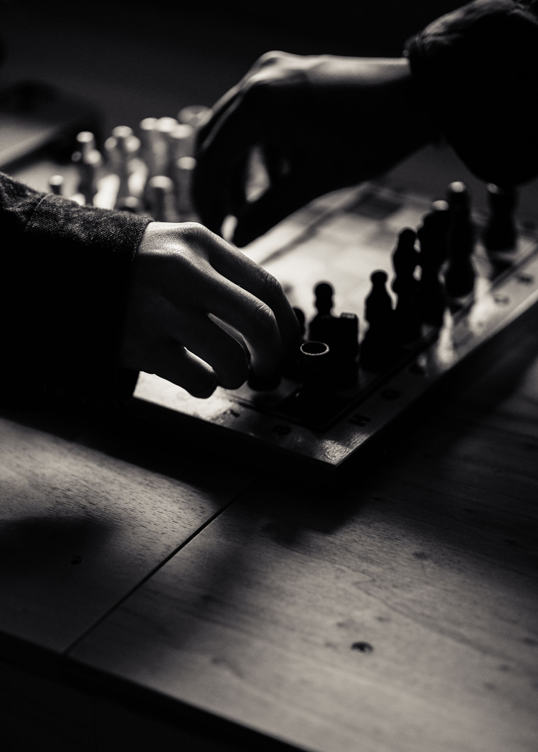 Illustrative photograph: A black-and-white close-up of hands and pieces on a wooden chessboard.