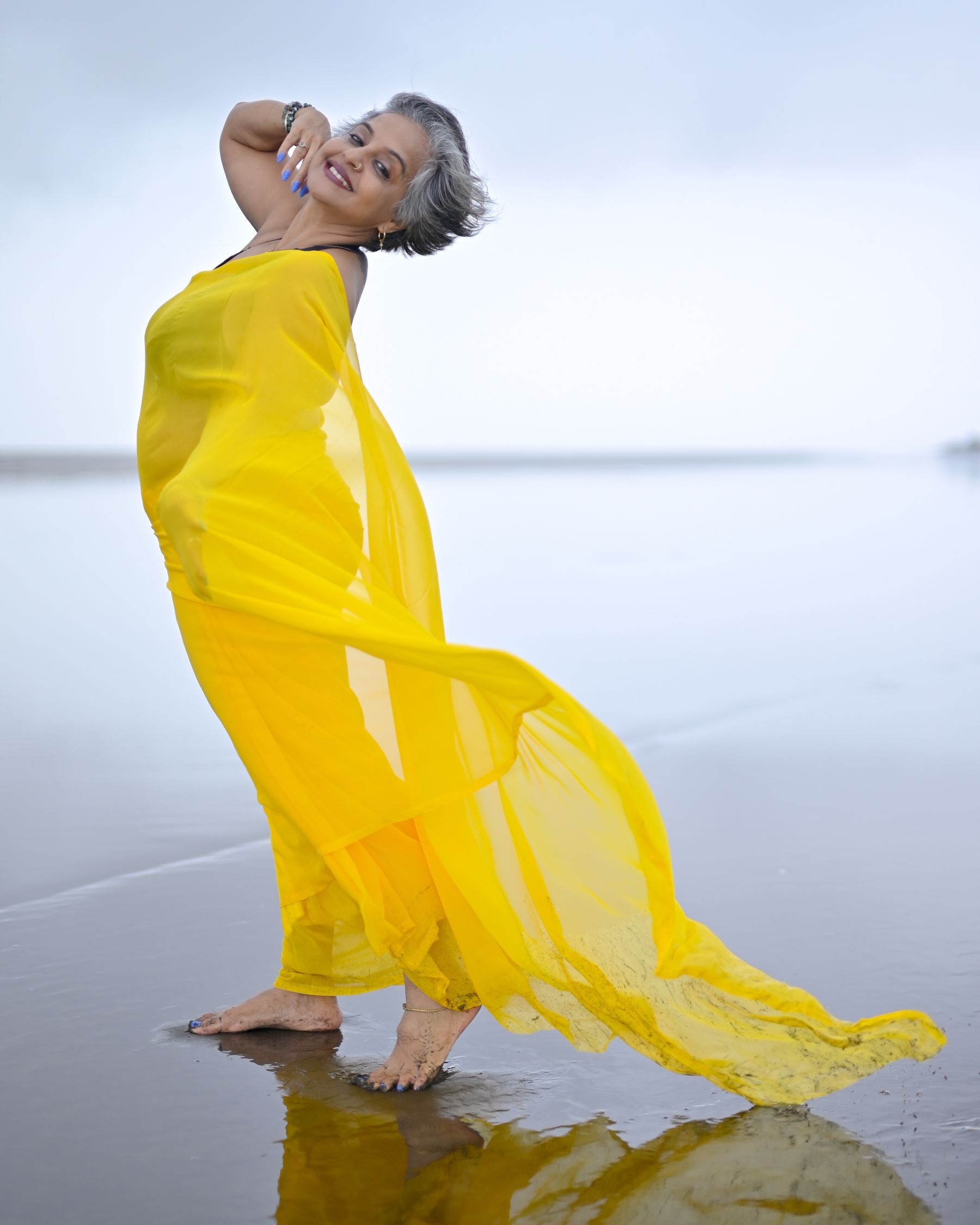 Illustrative photograph: A silver-haired woman in a flowing yellow dress enjoying the sea breeze on a Mumbai beach.